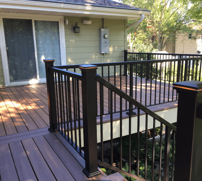 A deck with stairs and railing in the middle of it.