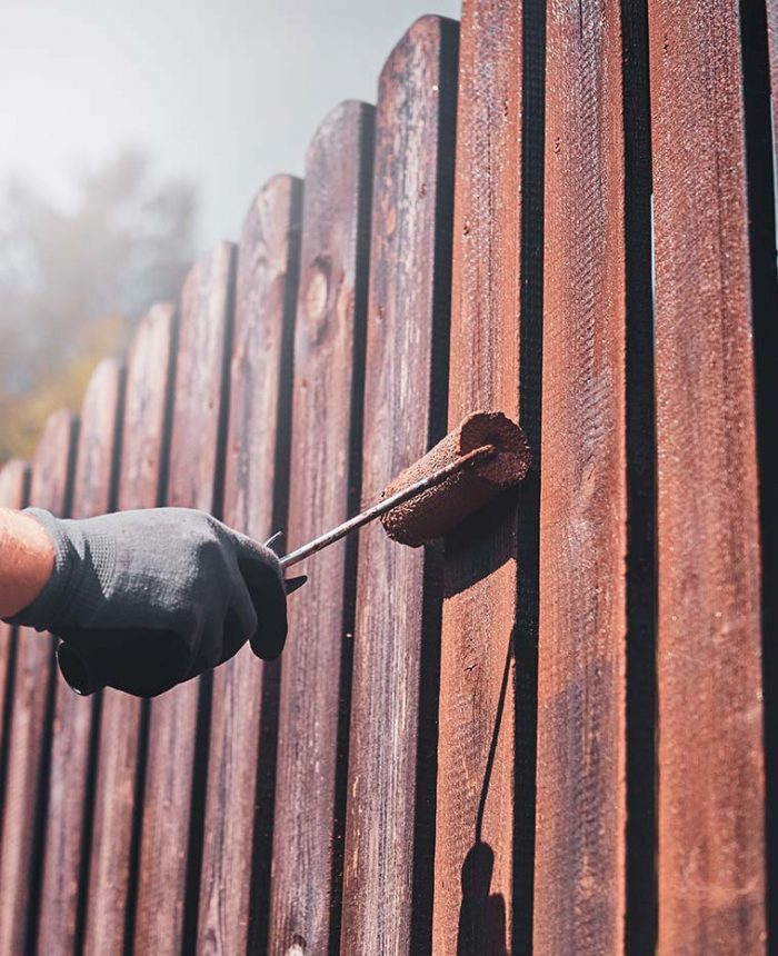 A person painting the side of a wooden fence.