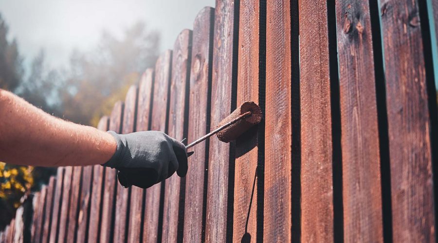 A person painting the side of a wooden fence.