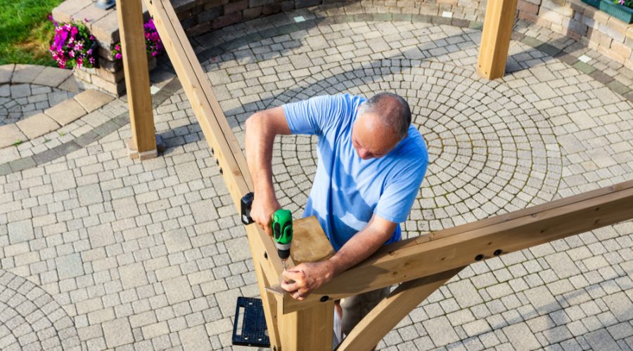 A man holding a beer bottle while standing on top of a wooden fence.