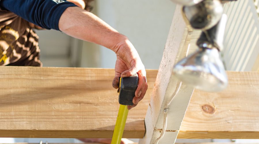 A person holding a yellow tape measure and a wooden board.