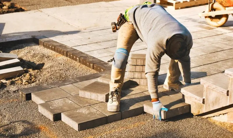 A person in knee pads and safety gear working on brick.