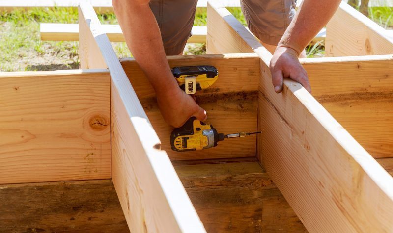 A person using a pair of drills to build a wooden structure.